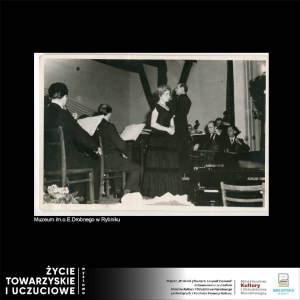 Scena, na której po środku stoi śpiewaczka w długiej sukni z krótkim rękawem. po lewej stronie siedzący tyłem muzycy, widać stojaki i zeszyty z nutami. Po prawej frontem muzycy z wiolonczelami. Na pierwszym planie widoczna część fortepianu. Zdjęcie czarno-białe wykonane w latach 50/60 tych.