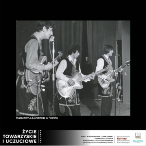 Na scenie stoją trzej mężczyźni z gitarami, w czarnych, długich kamizelkach, dwóch z nich śpiewa do stojących przed nimi mikrofonów. Zdjęcie czarno-białe wykonane w latach 50/60 tych.