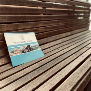 O oparcie drewnianej ławki oparty jest folder Politechniki Śląskiej ze zdjęciami kampusu, uczelni, insygniami oraz logiem.