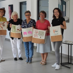 Zdjęcie przedstawia grupę pięciu kobiet stojących w jasnym wnętrzu.  Kobiety trzymają przed sobą torby na zakupy z namalowanymi ręcznie motywami. Jedna z kobiet ma torbę z napisem "Art Bridge". 