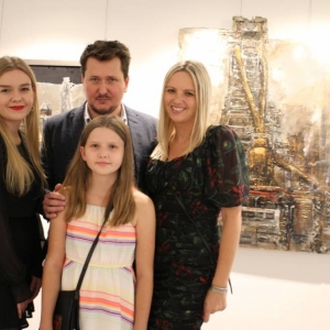 Na tle obrazów przedstawiające industrialny Śląsk stoi rodzina. Mężczyzna-autor wystawy wraz z żoną oraz nastolatka i dziewczynka.