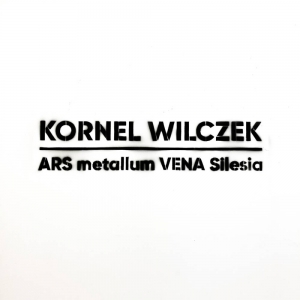 Na białej dykcie wysprejowany jest czarny napis Kornel Wilczek ARS Metallum VENA Silesia.