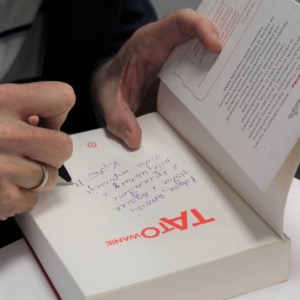 Zbliżenie na męskie dłonie wpisujące dedykację długopisem do książki "TATOwanie". 