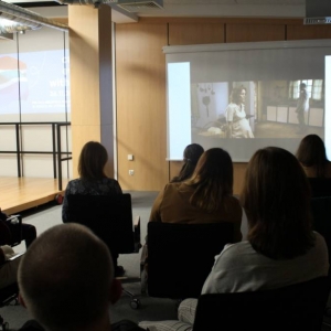 Ujęcie sali konferencyjnej z prawej strony. Na głównym ekranie wyświetlana jest grafika spotkania. Na jednym z bocznych ekranów fragment filmu. Film ogląda publiczność siedząca na krzesłach, panuje półmrok. 