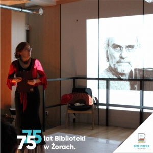 W sali konferencyjnej, przy przyciemnionych światłach, stoi kobieta ubrana w hiszpańskim stylu. Włosy ma upięte w kok, w dłoni trzyma podkładkę. Przed nią, na krzesłach siedzi publiczność. Za nią wyświetlane są zdjęcia mężczyzny z siwą brodą.W dole zdjęcia umieszczona jest  grafika z napisem 75 lat Biblioteki w  Żorach wraz z logiem umieszczonym w trójkącie w prawym dolnym rogu.