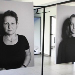 Na metalowej konstrukcji zawieszone na żyłkach są dwa czarno-białe zdjęcia wydrukowane na płytach PCV. Fotografie przedstawiają kobiety w wieku 25 i 60 lat. Kobiety spoglądają przed siebie i uśmiechają się.