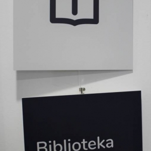 Zbliżenie na dwie tabliczki zawieszone na żyłce. Na jednej jest wydrukowany piktogram książki. Poniżej zawieszona jest tabliczka z napisem Biblioteka, Library.