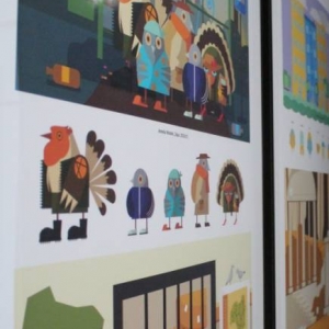 Fragment ściany, na której zawieszone są grafiki oprawione w ramki. Kilka grafik przedstawia nakładające się na siebie kolorowe figury, które tworzą graficzną całość. 